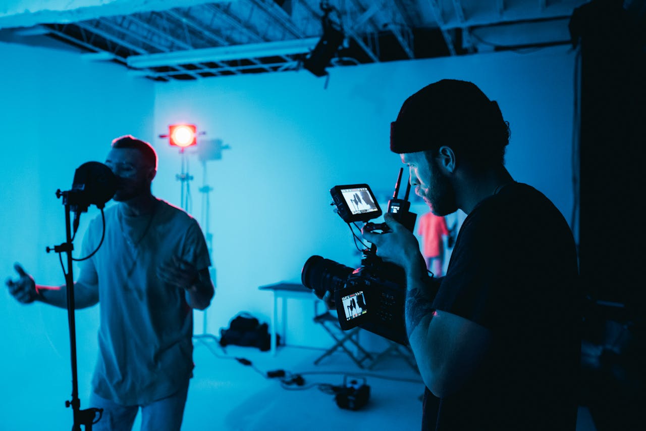 Male musician sings while videographer films in a studio setting.